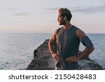 Small photo of Young strong sporty athletic toned fit sportsman man in sports clothes earphones warm up train with mobile phone akimbo at sunrise sun dawn over sea beach outdoor on pier seaside in summer day morning