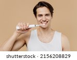 Small photo of Attractive cool young man he 20s perfect skin wearing undershirt hold brush brushing teeth isolated on plain pastel beige background studio portrait. Skin care healthcare cosmetic procedures concept.