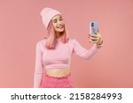 Small photo of Young woman 20s with bright dyed rose hair in rosy top shirt hat doing selfie shot on mobile cell phone isolated on plain light pastel pink background studio portrait. People lifestyle fashion concept