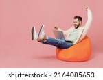 Full body young eacited overjoyed cool happy man in trendy jacket shirt sit in bag chair hold use work on laptop pc computer do winner gesture isolated on plain pastel light pink background studio.