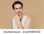 Small photo of Minded young man he 20s perfect skin in undershirt look aside on workspace area prop up chin isolated on pastel light beige background studio portrait. Skin care healthcare cosmetic procedures concept