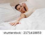 Smiling excited fun young woman in casual casual clothes lying in bed reach hand to camera you rest relax spend time in bedroom lounge home in own room house wake up dream be lost in reverie good day