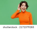 Small photo of Young curious nosy woman 20s wear casual orange turtleneck try to hear you overhear listening intently isolated on plain pastel light green color background studio portrait. People lifestyle concept