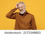 Small photo of Puzzled thoughtful wistful elderly gray-haired bearded man 50s years old wears brown shirt scratch on temple think lost in thought and conjectures isolated on plain yellow background studio portrait