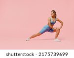 Small photo of Full size young sporty athletic fitness trainer woman wears blue tracksuit spend time in home gym train do stretch legs squat exercise isolated on pastel plain pink background. Workout sport concept