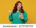 Small photo of Happy vivid excited young ginger chubby overweight woman 20s wears green shirt hold in hand use mobile cell phone celebrate clenching fists say yes isolated on plain yellow background studio portrait