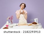 Small photo of Young wistful housewife housekeeper cook chef baker woman in pink apron work at table kitchenware hold cup coffee drink tea look aside isolated on pastel violet background Process cooking food concept
