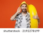 Small photo of Young tourist man wear beach shirt hat hold inflatable ring try to hear you overhear listening intently isolated on plain orange background studio portrait. Summer vacation sea rest sun tan concept