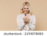 Fun elderly gray-haired blonde woman lady 40s years old wears pink dress hold in hand use mobile cell phone typing reading chatting searching isolated on plain pastel beige background studio portrait