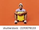 Full body traveler fun black man wear purple t-shirt hat sit hold suitcase isolated on plain orange color background. Tourist travel abroad in spare time rest getaway. Air flight trip journey concept