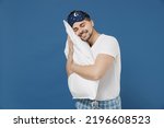 Side view young fun calm caucasian man 20s wearing pajama jam sleep mask rest relax at home hold hug pillow lying in bedroom isolated on dark blue background studio Good mood night bedtime concept.