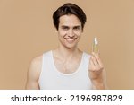 Small photo of Attractive young man he 20s perfect skin in undershirt hold bottle face body oil, moisturizing serum isolated on plain pastel beige background studio. Skin care healthcare cosmetic procedures concept