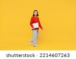 Full size body length fancy smiling happy young woman of Asian ethnicity 20s years old in casual clothes hold under hand laptop pc computer go move isolated on plain yellow background studio portrait