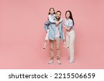 Small photo of Full body young parents mom dad with child kid daughter teen girl in blue clothes giving piggyback ride to kid, sit on back isolated on plain pastel light pink background Family day childhood concept