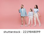 Small photo of Full body young happy parents mom dad with child kid daughter teen girl in blue clothes hold hands walk going point index finger aside on workspace area isolated on plain pastel light pink background.