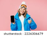 Snowboarder woman wear blue suit goggles mask hat ski jacket hold mobile cell phone blank screen show thumb up isolated on plain pastel pink background. Winter extreme sport hobby trip relax concept