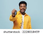 Young smiling happy fun man of African American ethnicity 20s wear yellow shirt hold giving car keys fob keyless system isolated on plain pastel light blue background studio. People lifestyle concept