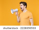 Small photo of Young unshaved angry protestive agitating caucasian man 20s in casual basic t-shirt screaming shouting loudly in megaphone bullhorn looking aside isolated on yellow color background studio portrait
