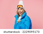 Side view snowboarder woman wear blue suit goggles mask hat ski padded jacket do winner gesture celebrate isolated on plain pastel pink background Winter extreme sport hobby weekend trip relax concept