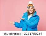 Snowboarder happy woman wear blue suit goggles mask hat ski padded jacket point arms hands aside on area isolated on plain pastel pink background. Winter extreme sport hobby weekend trip relax concept