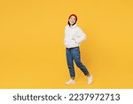 Full body side view cheerful young woman of Asian ethnicity wear white padded windbreaker jacket red hat walk go look aside on workspace isolated on plain yellow background People lifestyle concept