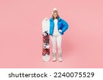Full body snowboarder woman wear blue suit goggles mask hat ski padded jacket hold snowboard stand akimbo isolated on plain pastel pink background Winter extreme sport hobby weekend trip relax concept