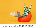 Small photo of Full body young latin IT woman wears casual cozy green knitted sweater sit in bag chair hold use work on laptop pc computer do winner gesture raise up hands isolated on plain yellow background studio
