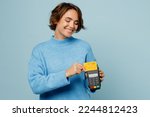Young caucasian woman wear knitted sweater hold wireless modern bank payment terminal to process acquire credit card isolated on plain pastel light blue cyan background studio People lifestyle concept