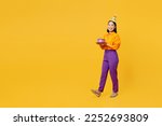 Full body side view happy smiling fun young woman wears casual clothes hat celebrating hold in hand cake with candles walk go isolated on plain yellow background. Birthday 8 14 holiday party concept