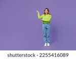Full body young fun woman 30s she wearing casual green knitted sweater point index finger aside indicate on workspace area copy space mock up isolated on plain pastel purple background studio portrait