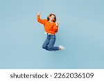 Small photo of Full body young woman of Asian ethnicity wear orange sweater glasses headphones listen to music raise up hands dance jump high use mobile cell phone isolated on plain pastel light blue cyan background