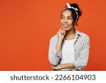 Young woman of African American ethnicity she wears grey shirt headband put hand prop up on chin, lost in thought and conjectures isolated on plain orange background studio. People lifestyle concept