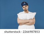 Small photo of Young disappointed displeased man 20s in pajama jam sleep mask rest relax at home hold hug pillow lying in bedroom look camera isolated on dark blue background studio Bad mood night bedtime concept.