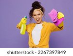 Young confident cool housekeeper woman 20s wear yellow shirt tidy up hold in hand bottle spray detergent rag microfiber cloth isolated on plain pastel light purple background studio Housework concept