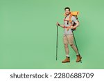 Small photo of Full size young traveler white man carry backpack stuff mat walk with trakking poles isolated on plain green background. Tourist leads active healthy lifestyle. Hiking trek rest travel trip concept