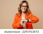 Young smiling happy fun successful employee business woman corporate lawyer 30s wear classic formal orange suit glasses smart watch check time work in office isolated on plain beige background studio