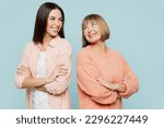 Small photo of Smiling fun elder parent mom with young adult daughter two women together wearing casual clothes hold hands crossed folded look to each other isolated on plain blue cyan background. Family day concept