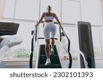 Small photo of Back view full size young strong sporty athletic sportswoman woman in white sportswear warm up training running on a treadmill climber stairs machine in gym indoors. Workout sport motivation concept