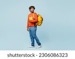 Full body side view young teen Indian boy student he wearing casual clothes backpack bag hold books walk go looka aside isolated on plain pastel blue background. High school university college concept