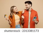 Small photo of Young couple two friends family man woman wear casual clothes using mobile cell phone credit bank card shopping online order delivery booking tour hugging together isolated on plain beige background