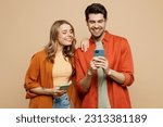 Young smiling happy couple two friends family man woman wear casual clothes hold in hand use mobile cell phone together chatting isolated on pastel plain light beige color background studio portrait