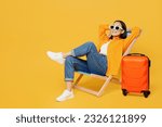 Young calm woman wear summer clothes sit in deckchair hold hands behind neck isolated on plain yellow background. Tourist travel abroad in free spare time rest getaway. Air flight trip journey concept
