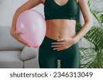 Small photo of Cropped close up young strong sporty athletic fitness trainer instructor woman wear green tracksuit training hold balloon near belly do exercises at home gym indoor. Workout sport motivation concept