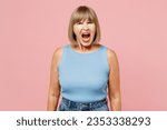 Small photo of Elderly angry mad sad furious indignant blonde woman 50s years old she wears blue undershirt casual clothes look camera scream shout isolated on plain pastel light pink background. Lifestyle concept