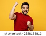 Small photo of Young excited happy Indian man he wears red t-shirt casual clothes doing winner gesture celebrate clenching fists say yes isolated on plain yellow orange background studio portrait. Lifestyle concept