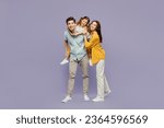Small photo of Full body young joyful happy parents mom dad with child kid daughter girl 6 years old wear blue yellow casual clothes giving piggyback ride to joyful, sit on back isolated on plain purple background