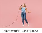 Small photo of Full body singer elderly blonde woman 50s years old she wears blue undershirt casual clothes sing song in microphone at karaoke club isolated on plain pastel light pink background . Lifestyle concept