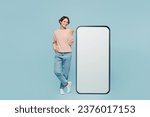 Small photo of Full body young woman wear beige knitted sweater casual clothes point index finger on big huge blank screen mobile cell phone smartphone with workspace area isolated on plain pastel blue background