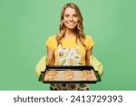 Young housewife housekeeper chef cook baker woman wears apron yellow t-shirt hold chocolate cookies on baking tray look camera isolated on plain pastel green background studio. Cooking food concept