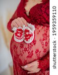 Small photo of a pregnant woman in a bright negligee holds booties in her hands